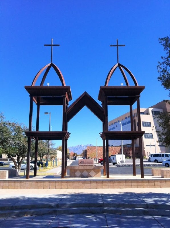 Modern rusting monument to St. Genevieve with twin crosses and the Organ Mountains behind it.
